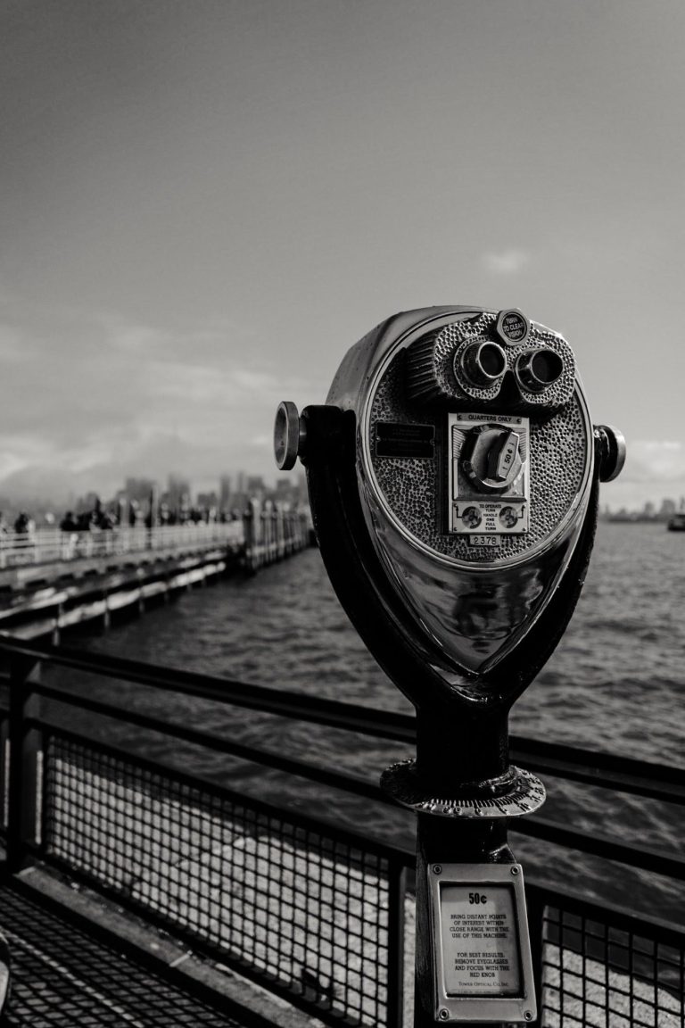 Black and white image of sightseeing binoculars on the pier, representing taking a closer look.